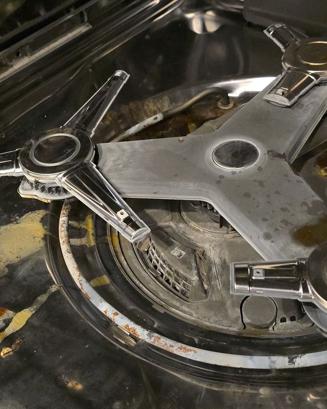 Bottom of a dishwasher tub with the spray arms and filter area, showing food residue