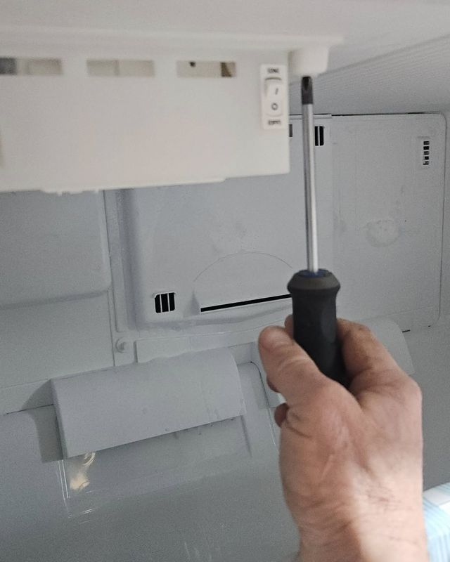 A hand holding a screwdriver inside a refrigerator during a repair